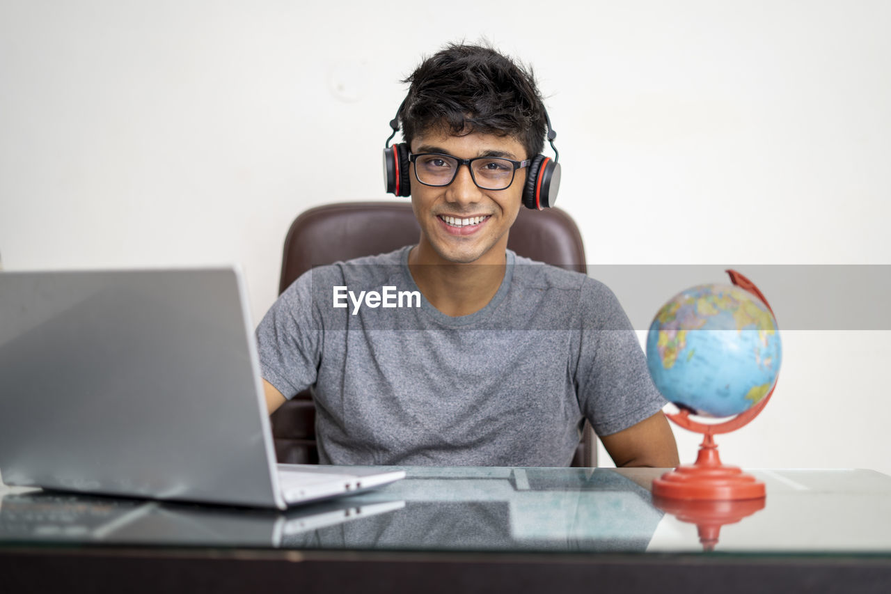 PORTRAIT OF SMILING YOUNG MAN USING LAPTOP