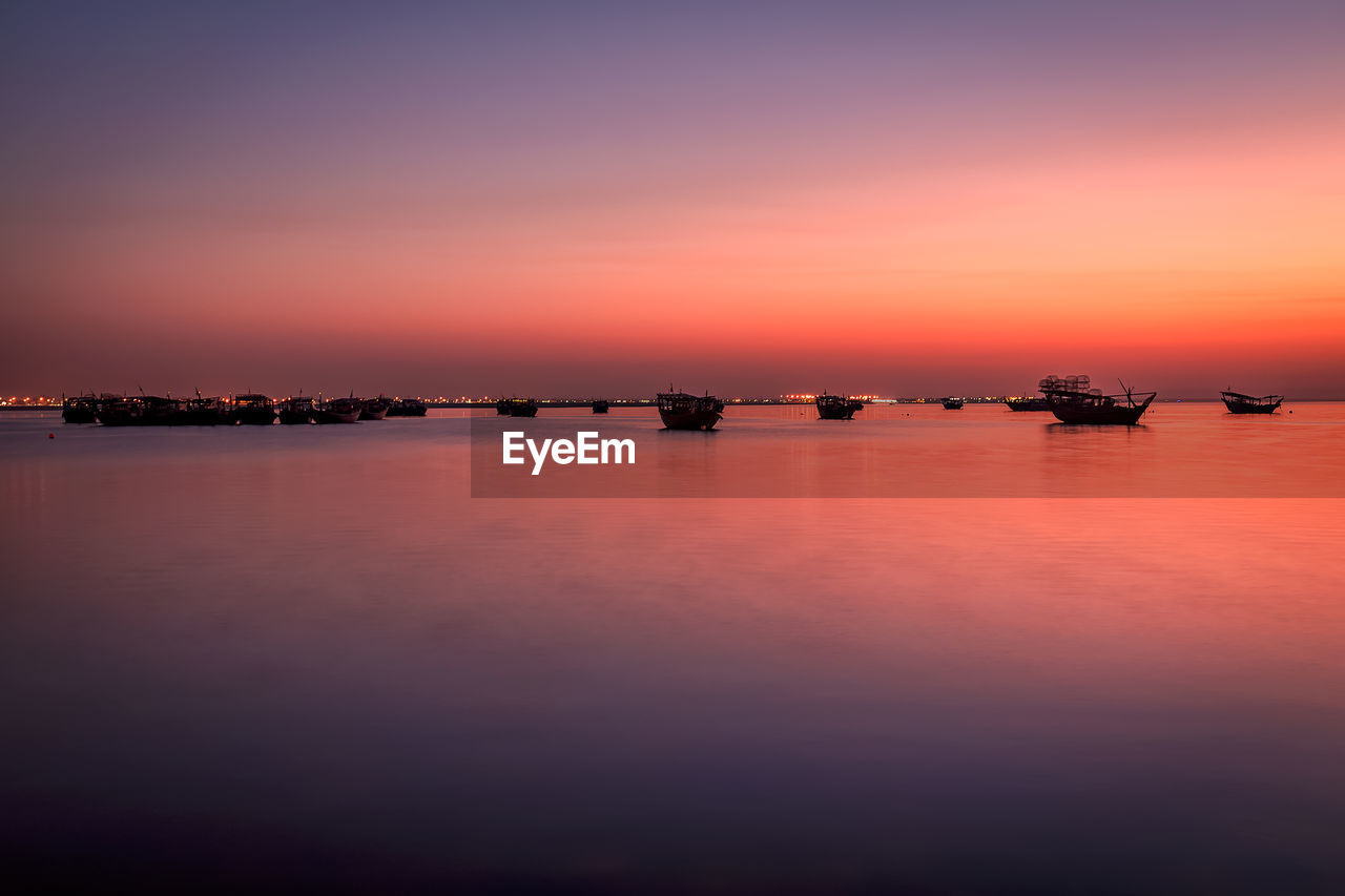 SILHOUETTE BOATS IN SEA AGAINST ORANGE SKY