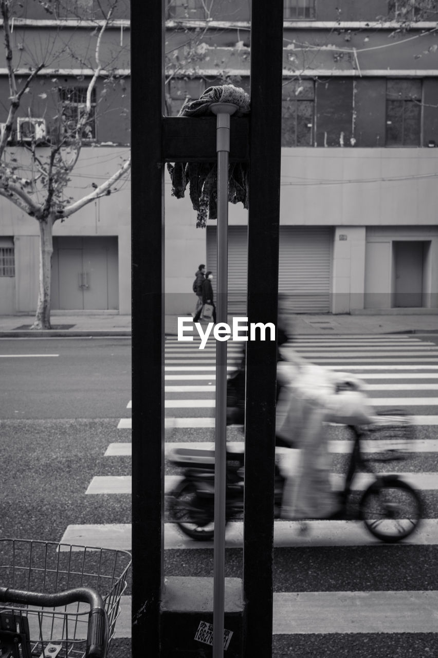 BLURRED MOTION OF PEOPLE RIDING MOTORCYCLE ON STREET AGAINST BUILDING