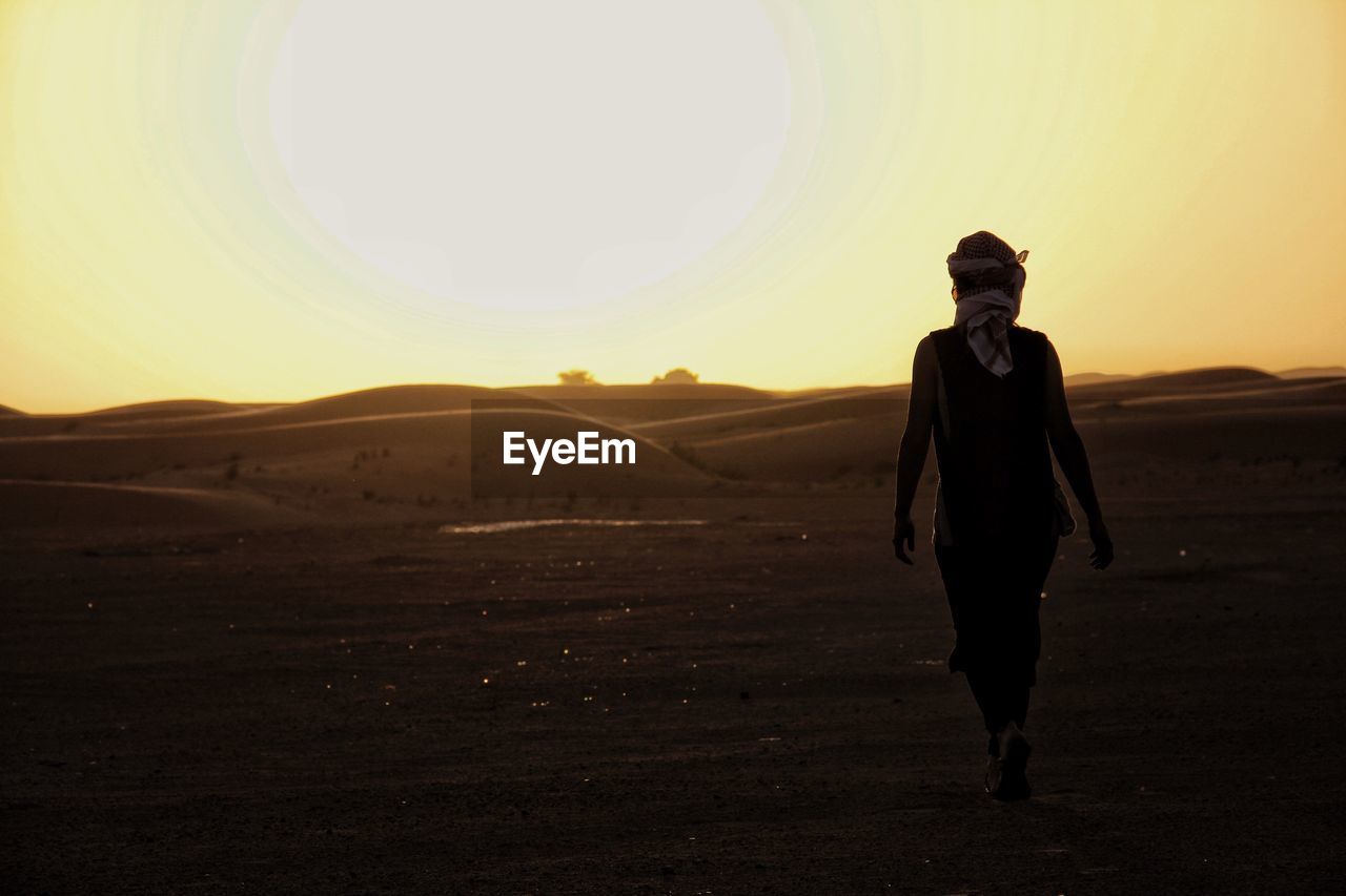 Silhouette of man walking in desert during sunset