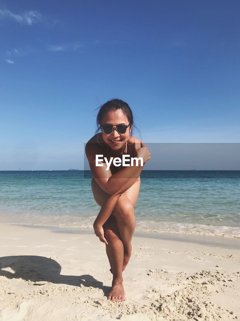 Full length of woman wearing bikini while practicing yoga at beach against sky