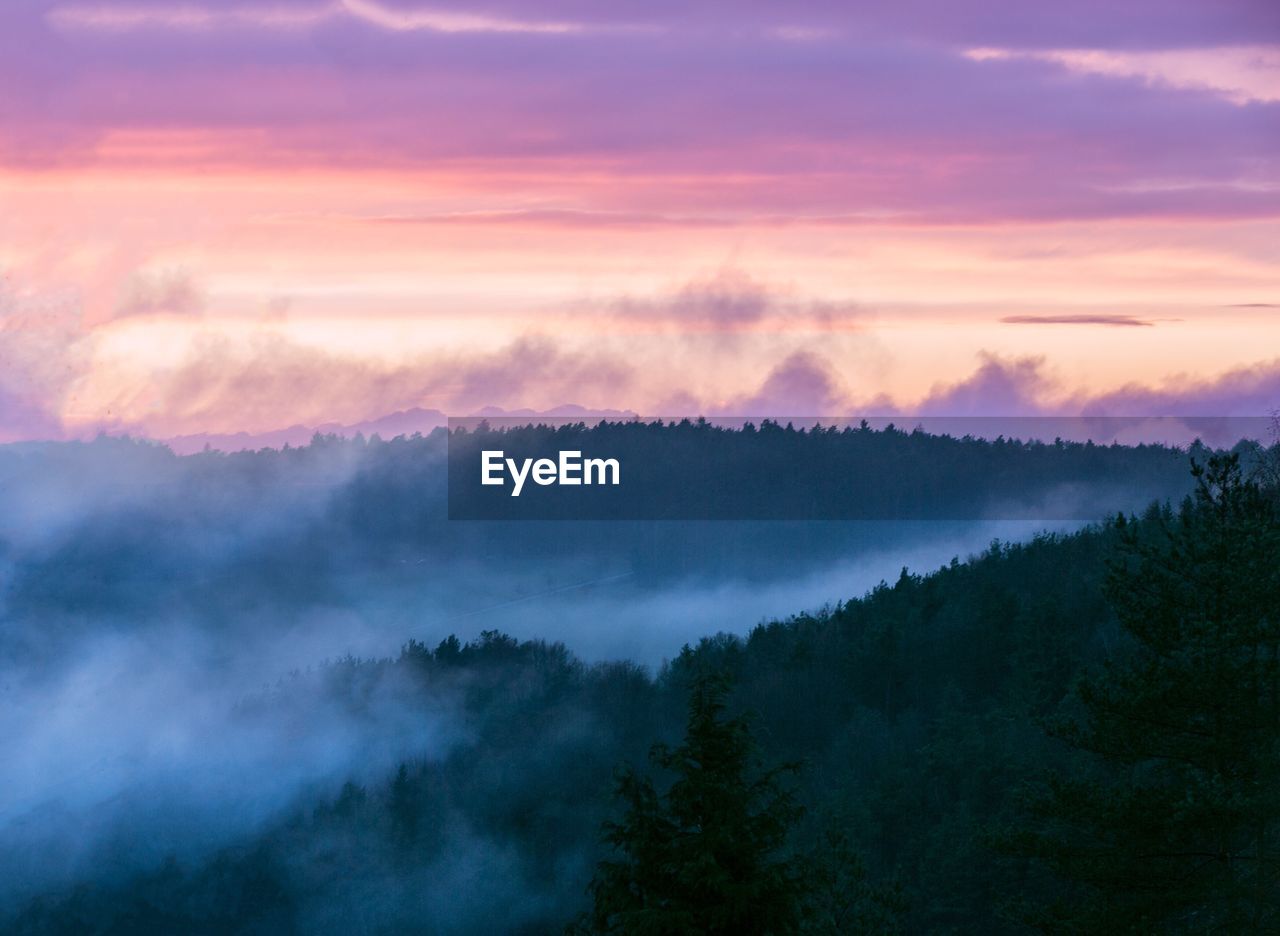 Scenic view of mountains against cloudy sky during foggy weather at sunset