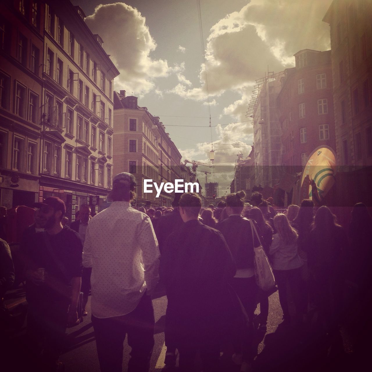 Rear view of people walking on road amidst buildings against cloudy sky