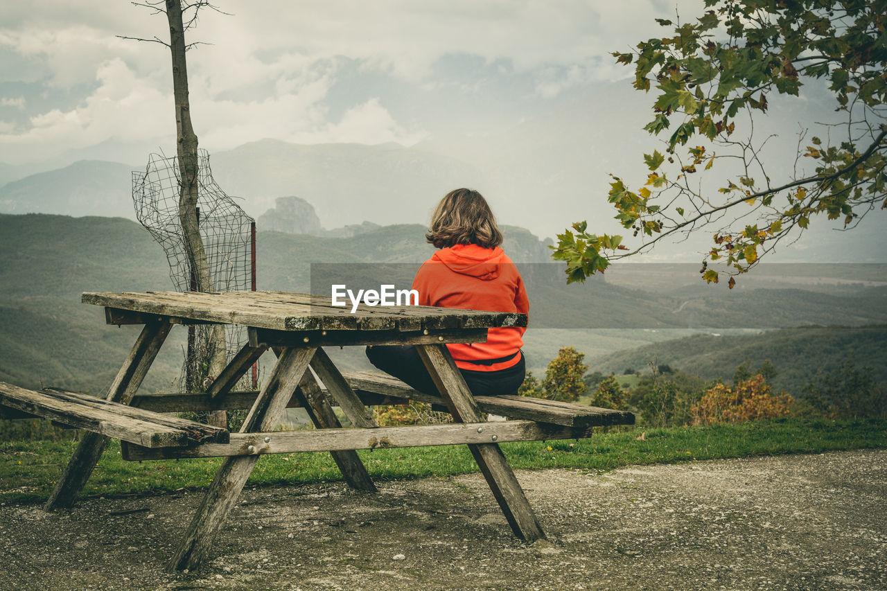 Rear view of man sitting on picnic table against mountains