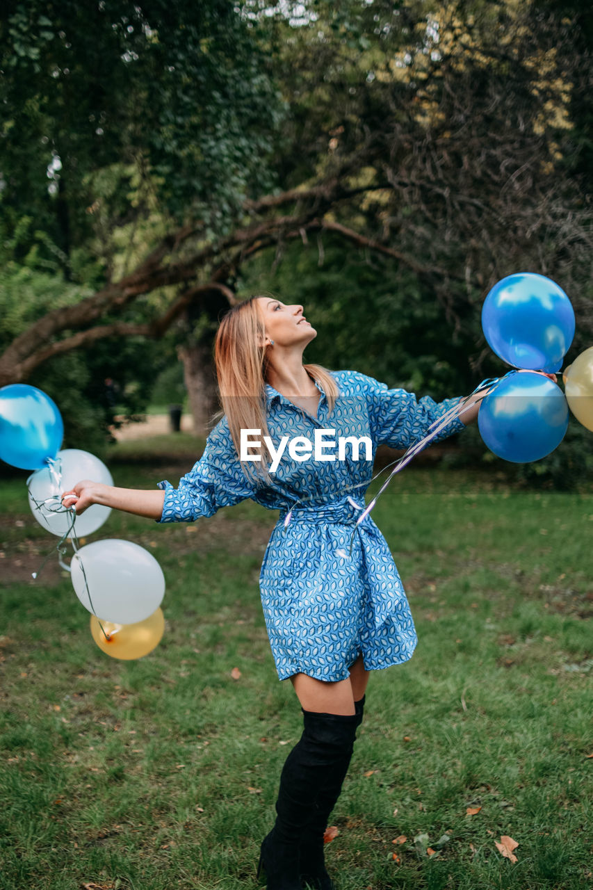 REAR VIEW OF WOMAN HOLDING BALLOONS ON GRASSLAND