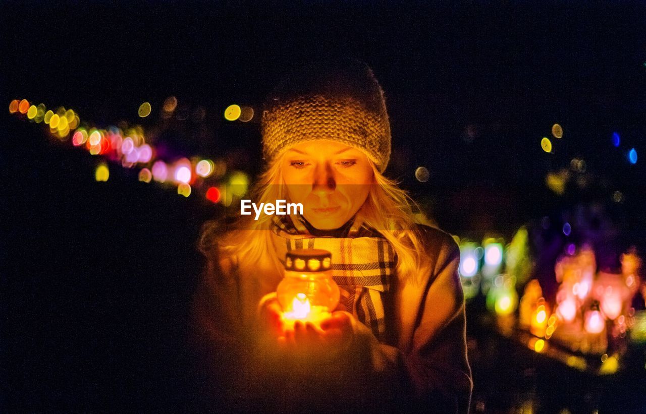 Close-up woman holding illuminated oil lamp at night