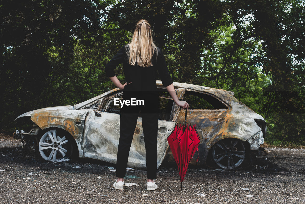 REAR VIEW OF PERSON STANDING BY CAR ON TREE