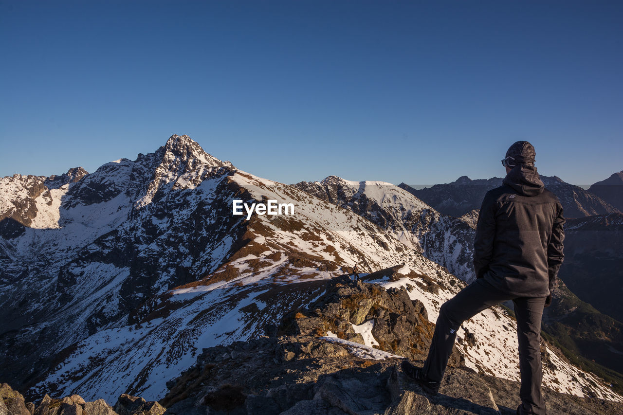 Rear view of man standing on rocky mountains against clear sky