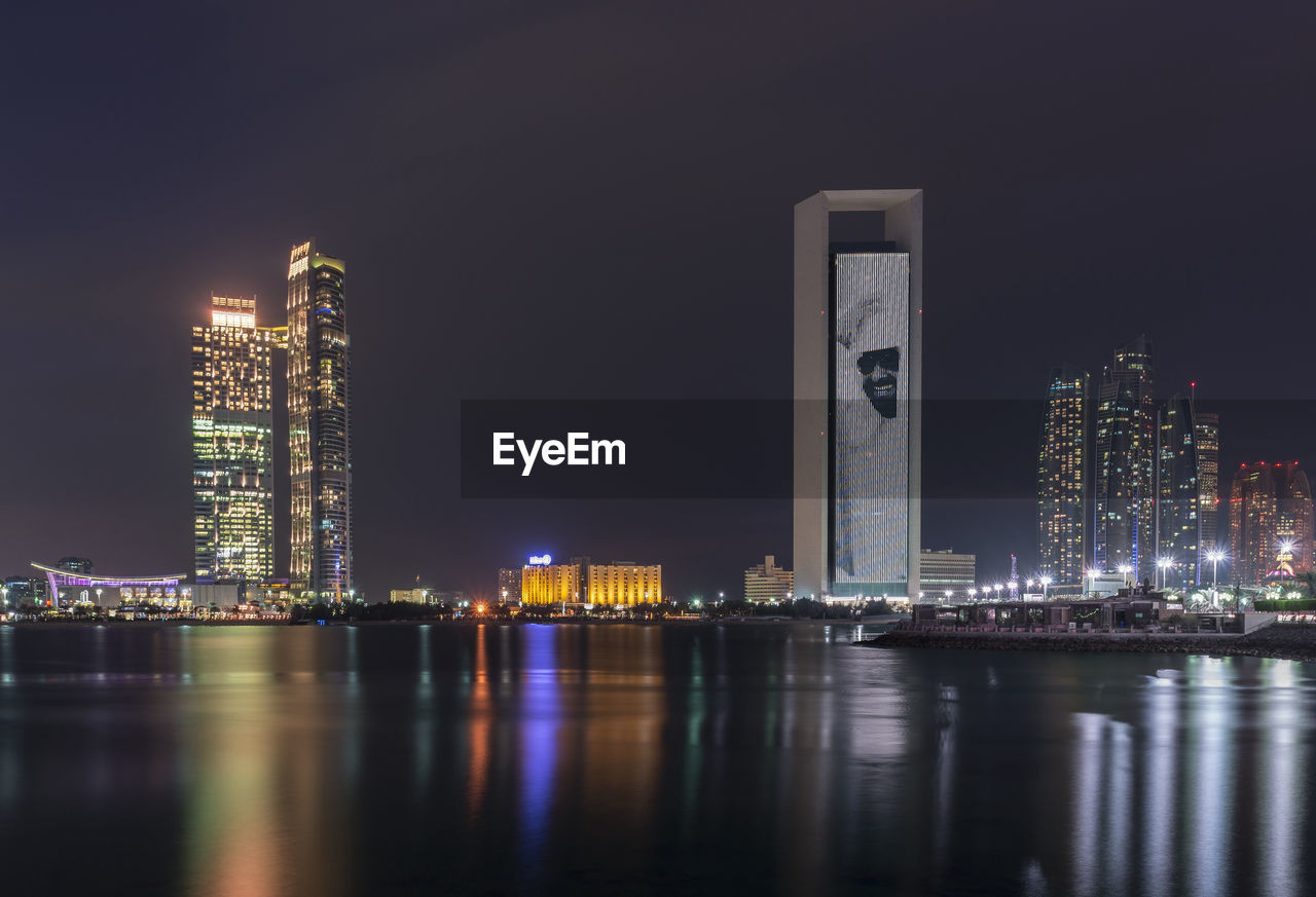 RIVER BY ILLUMINATED BUILDINGS AGAINST SKY AT NIGHT