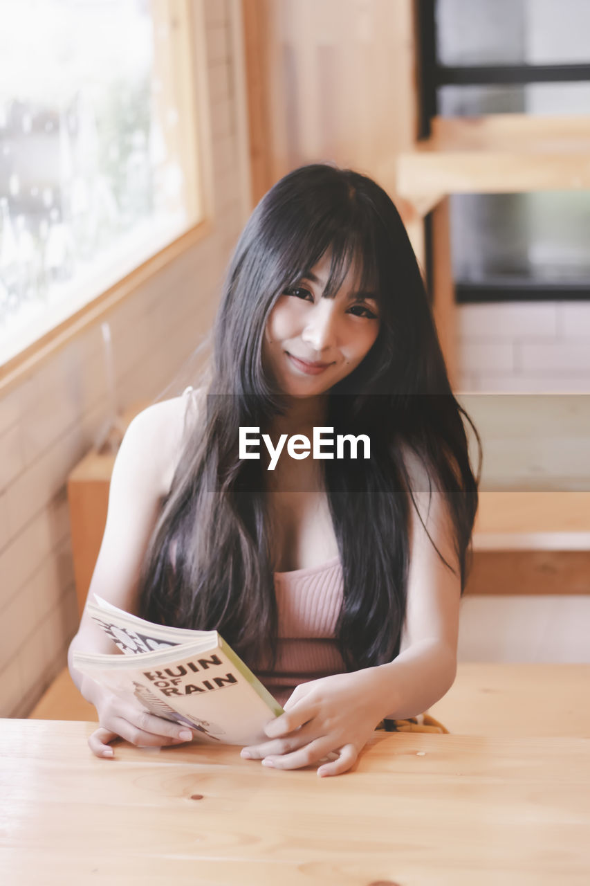 PORTRAIT OF SMILING WOMAN SITTING AT TABLE