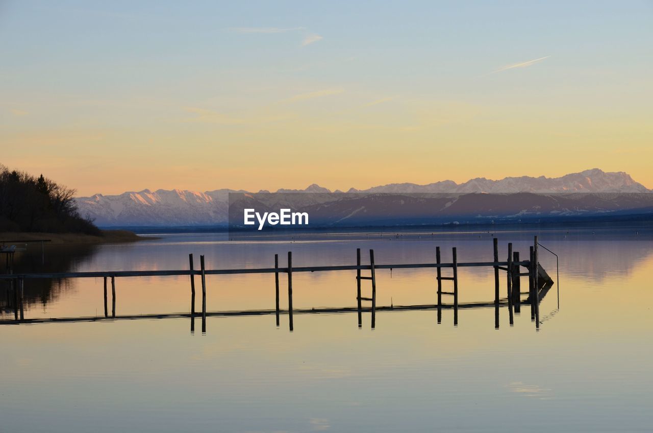 Wooden posts in lake against sky during sunset