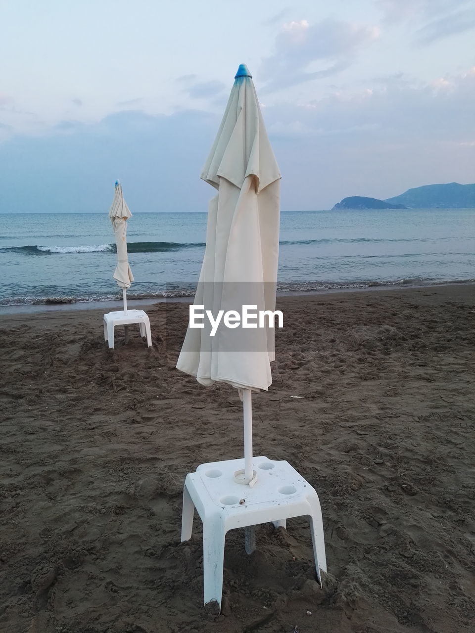 Closed parasols at beach against cloudy sky