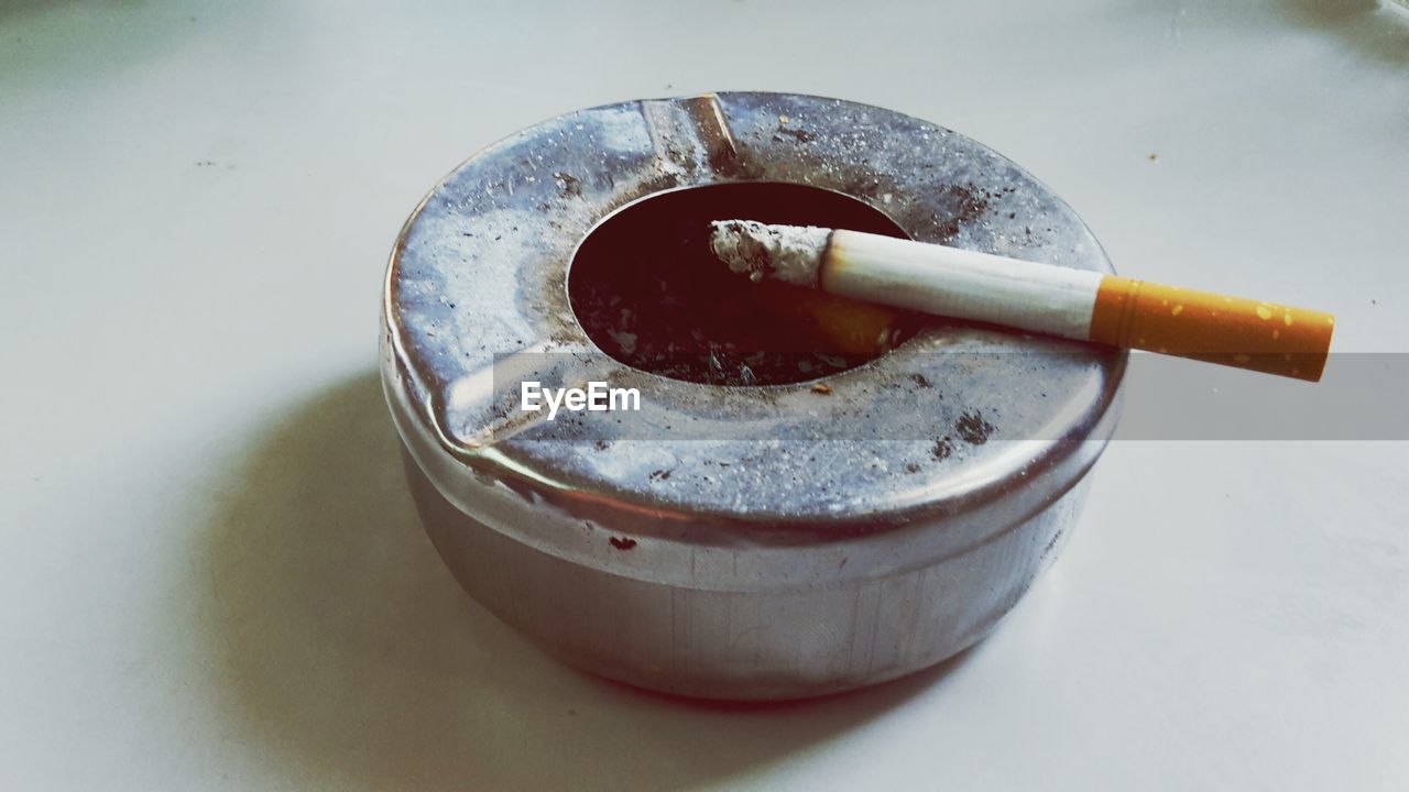 Close-up of cigarette in metallic ash tray on floor