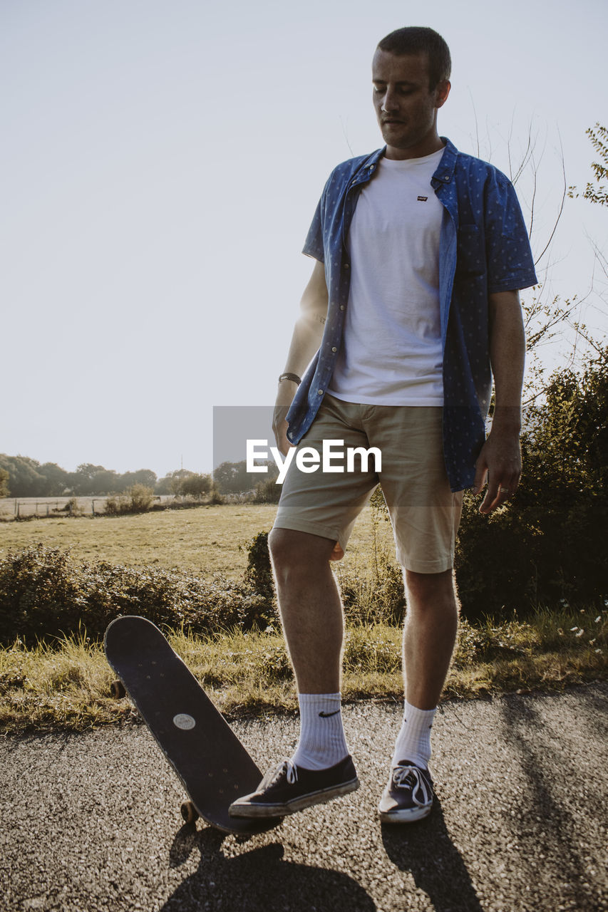 Full length of man standing with skateboard on road against sky