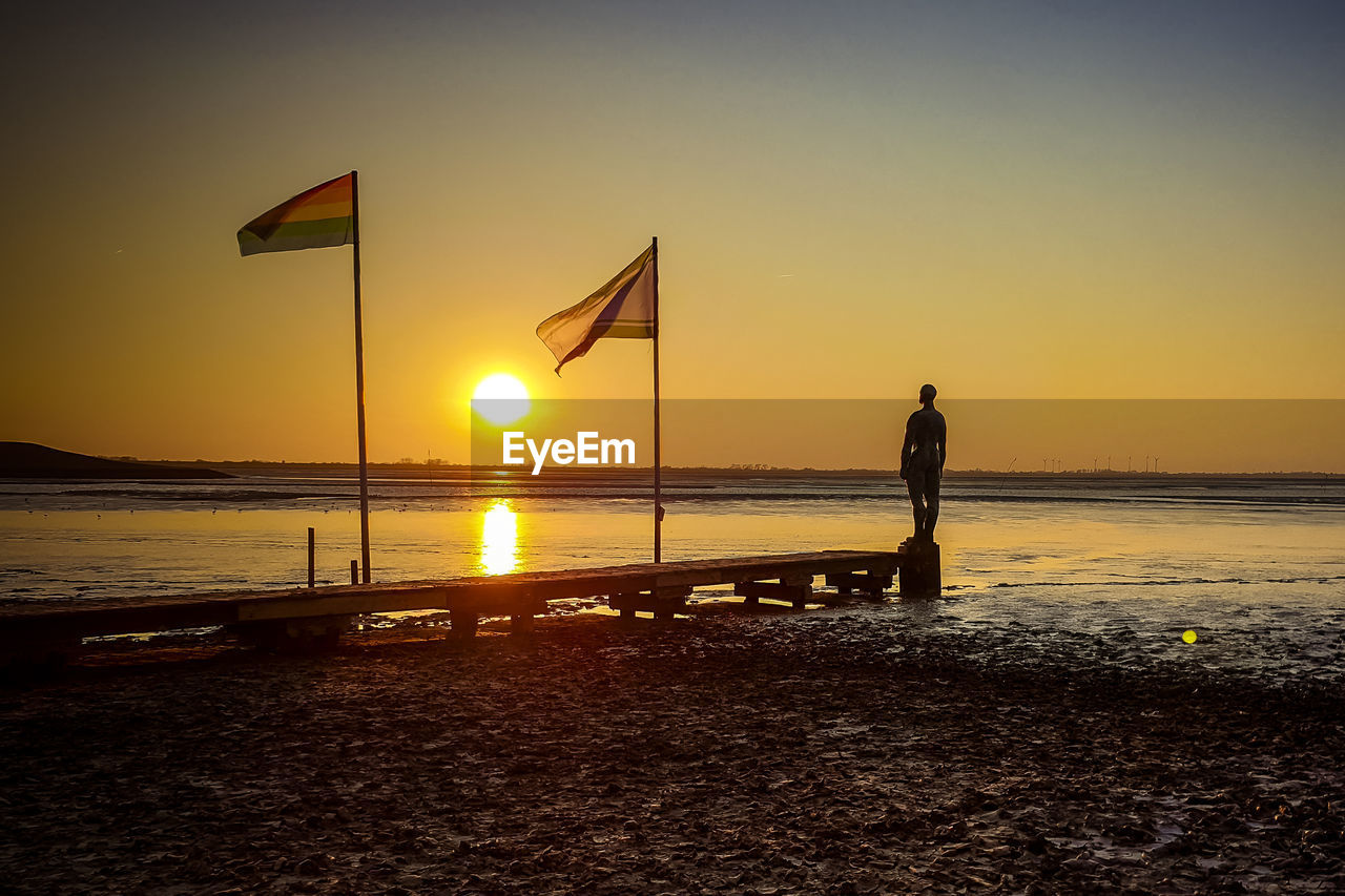 Silhouette man standing on beach against sky during sunset