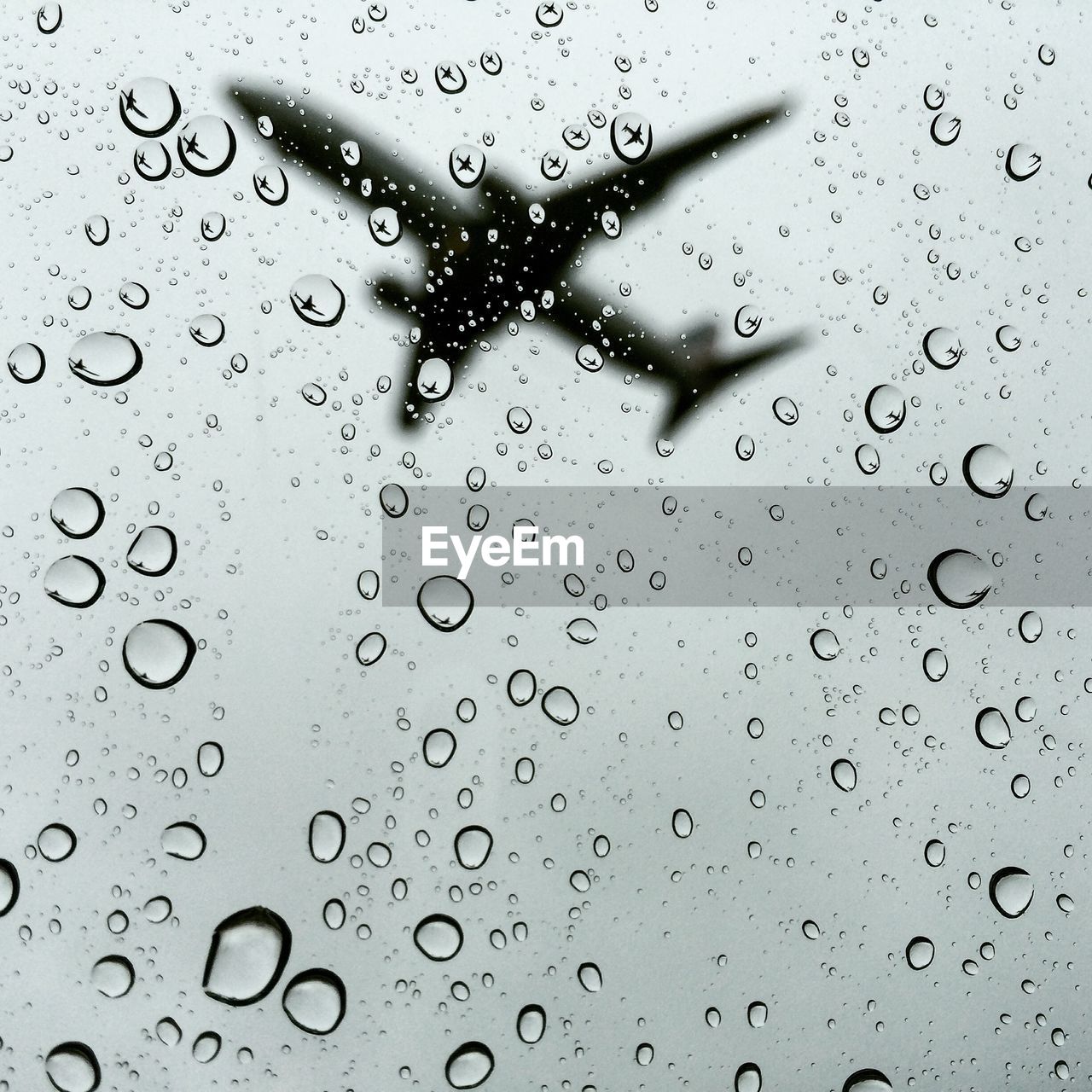 Low angle view of airplane flying against sky seen through wet window