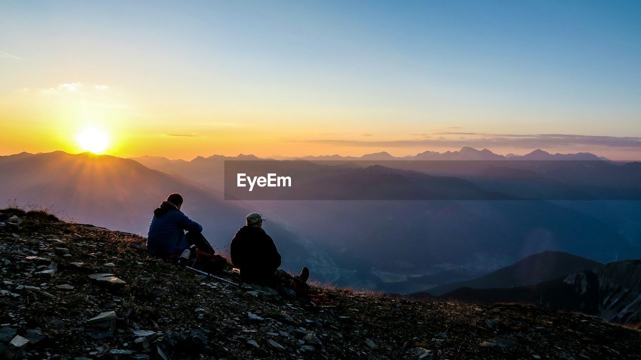 Friends sitting on mountain at sunset