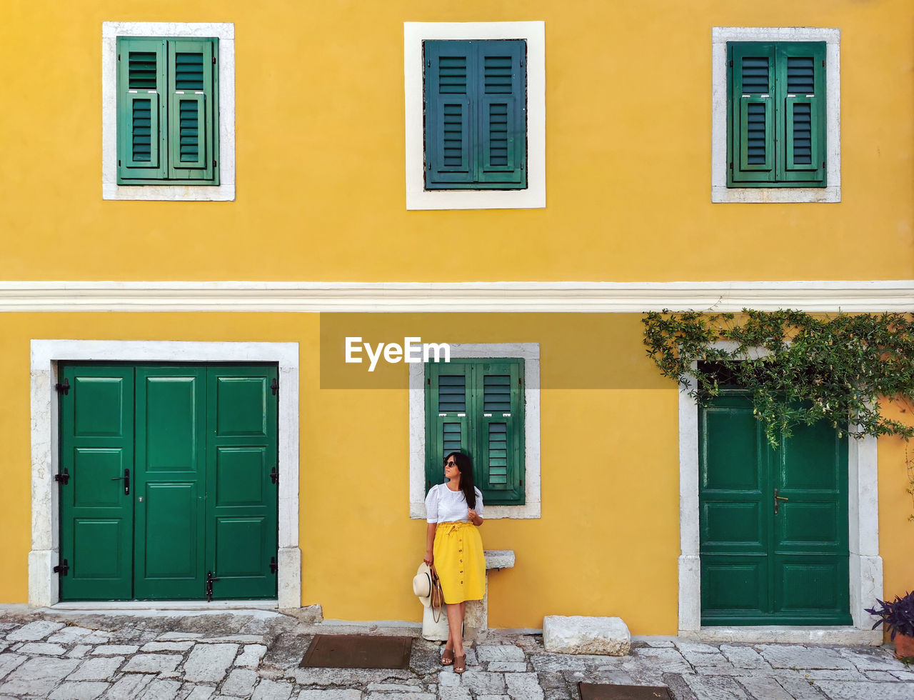 Young woman in summer outfit standing in front of yellow house.