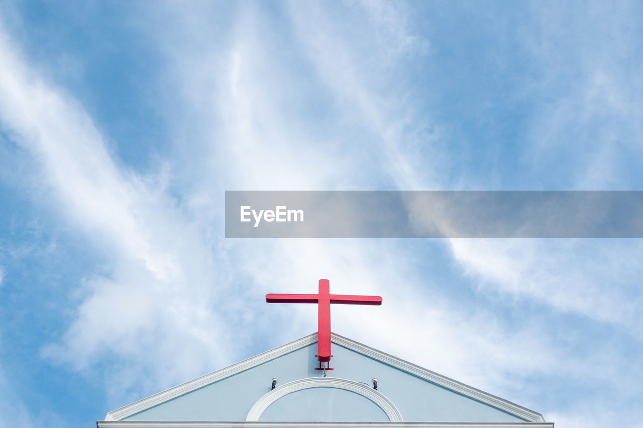 Church roof with red cross and blue sky.