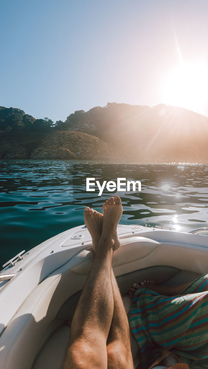 water, relaxation, nature, vacation, sunlight, sky, trip, holiday, one person, sea, boat, adult, travel, sun, leisure activity, human leg, boating, personal perspective, summer, lifestyles, transportation, tranquility, low section, nautical vessel, vehicle, barefoot, human limb, clear sky, day, beauty in nature, adventure, land, travel destinations, watercraft, limb, scenics - nature, outdoors, lens flare, tranquil scene, sunset, ocean, mode of transportation, men, mountain, sunny, human foot, beach, sunbeam, enjoyment, women, lying down, copy space, resting, blue