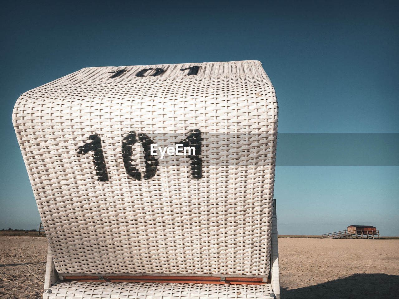 Traditional north german white beach chair with black number 101 at north sea beach against blue sky