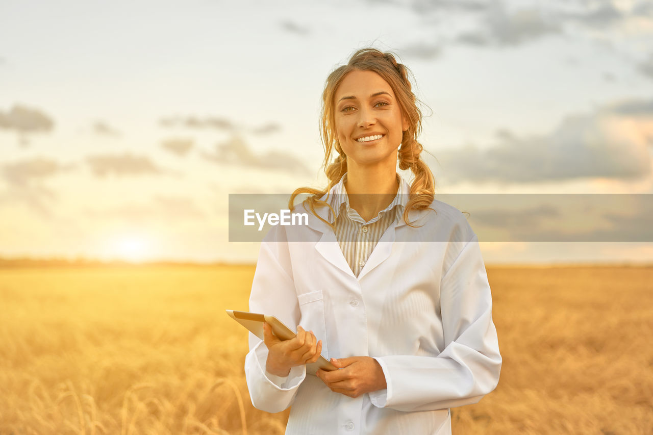 PORTRAIT OF SMILING YOUNG WOMAN STANDING IN FIELD