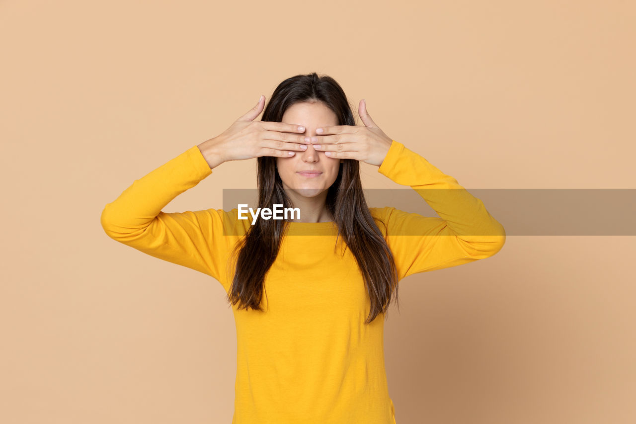 PORTRAIT OF YOUNG WOMAN STANDING AGAINST YELLOW WALL