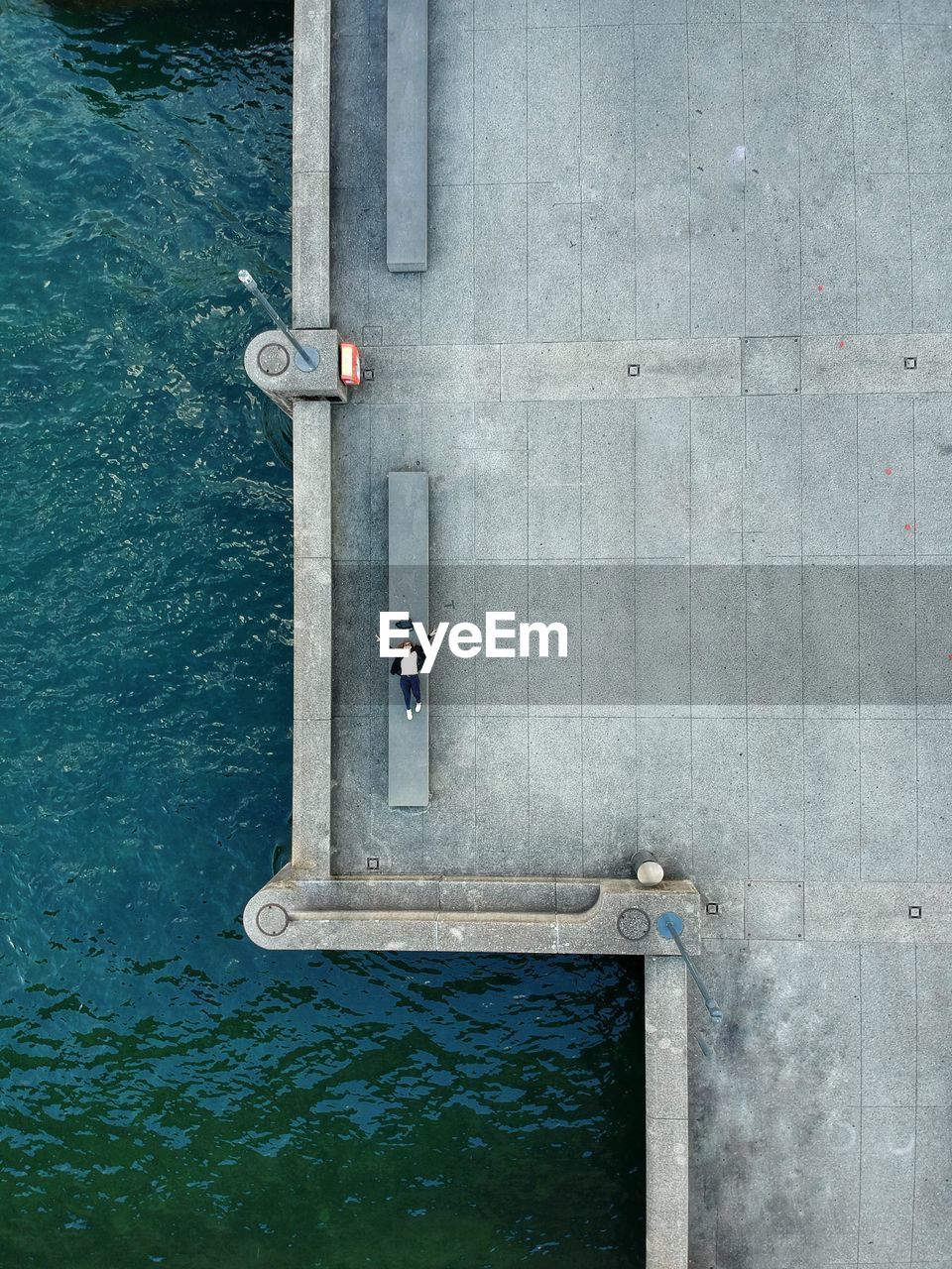 High angle view of woman lying on bench at promenade by sea