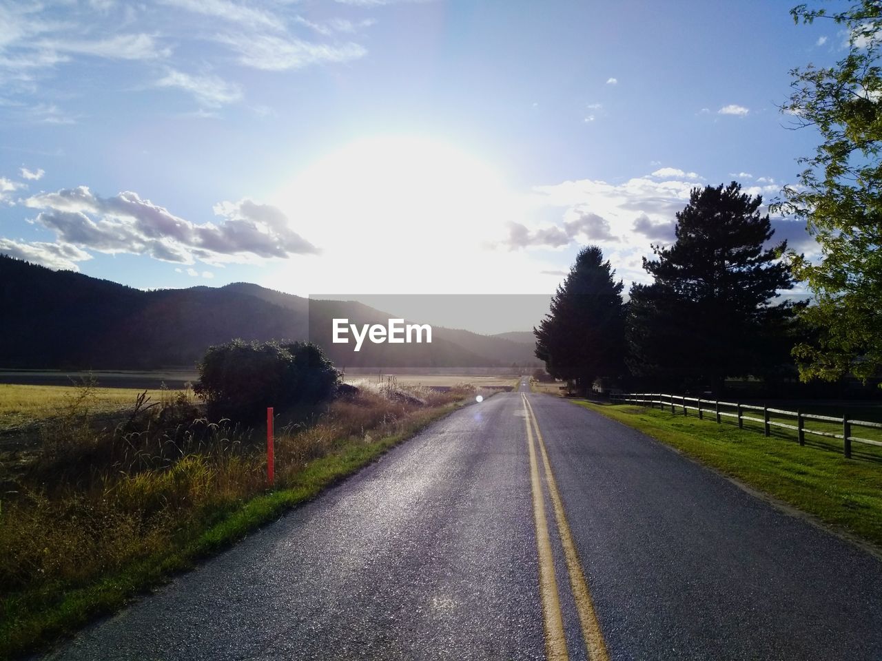 Empty road along trees and mountains against sky