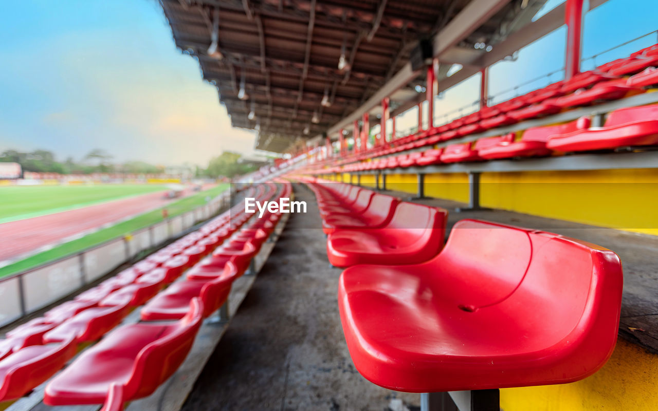 Empty red seat on grandstand for fans cheering at football stadium with evening sky