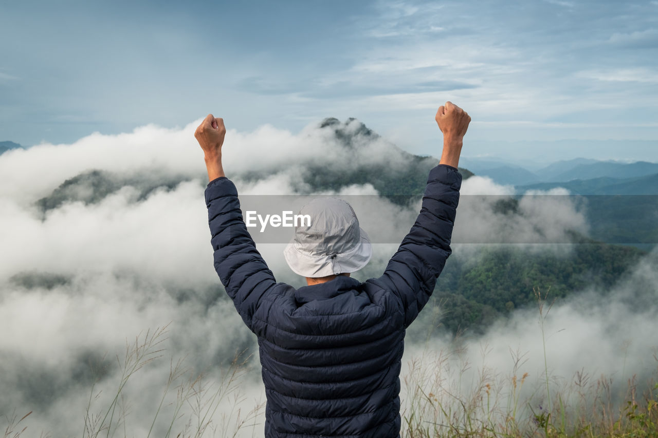 Rear view of man with arms raised while standing on mountain against sky