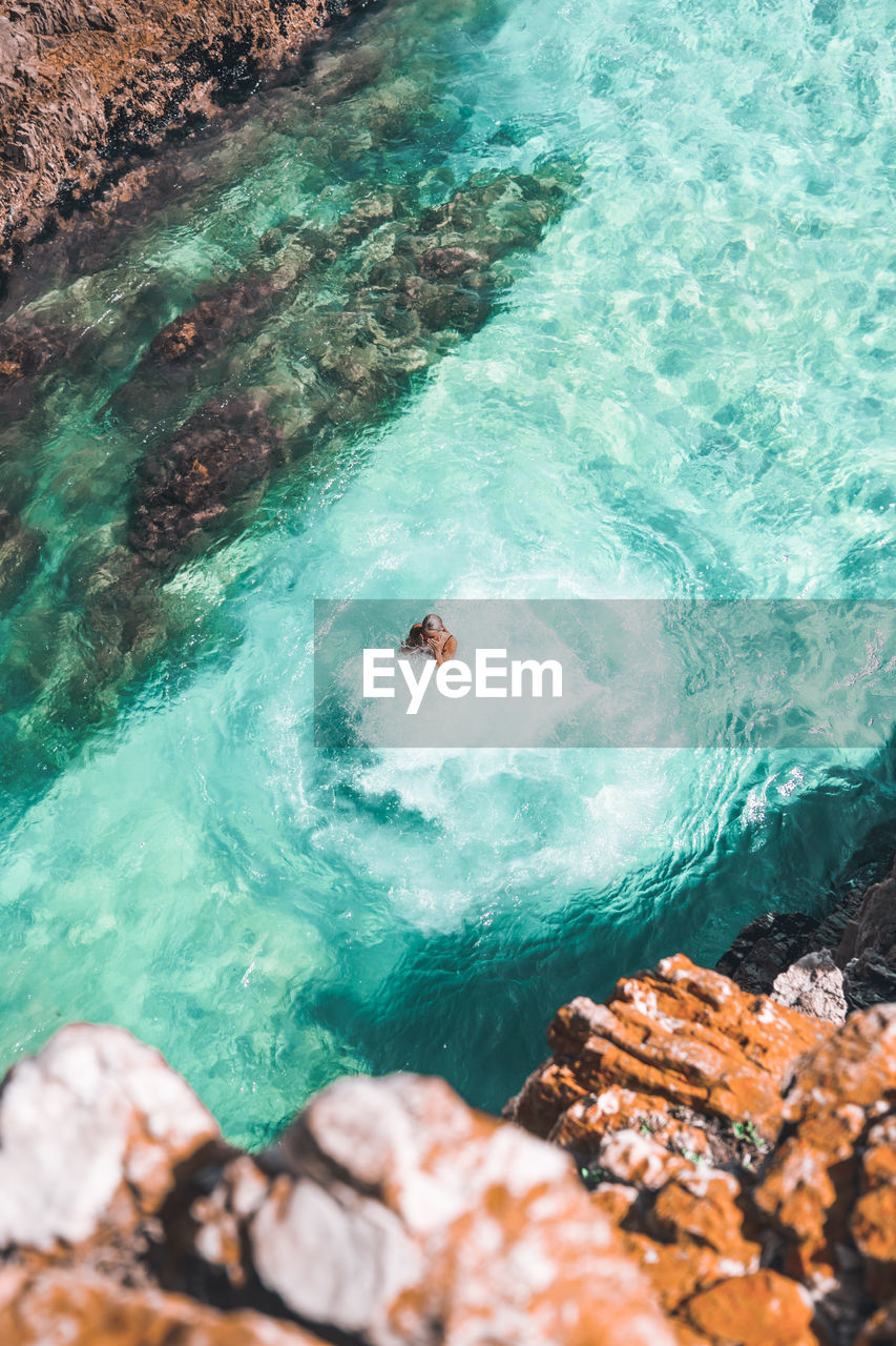 HIGH ANGLE VIEW OF PEOPLE SWIMMING ON ROCKS IN SEA