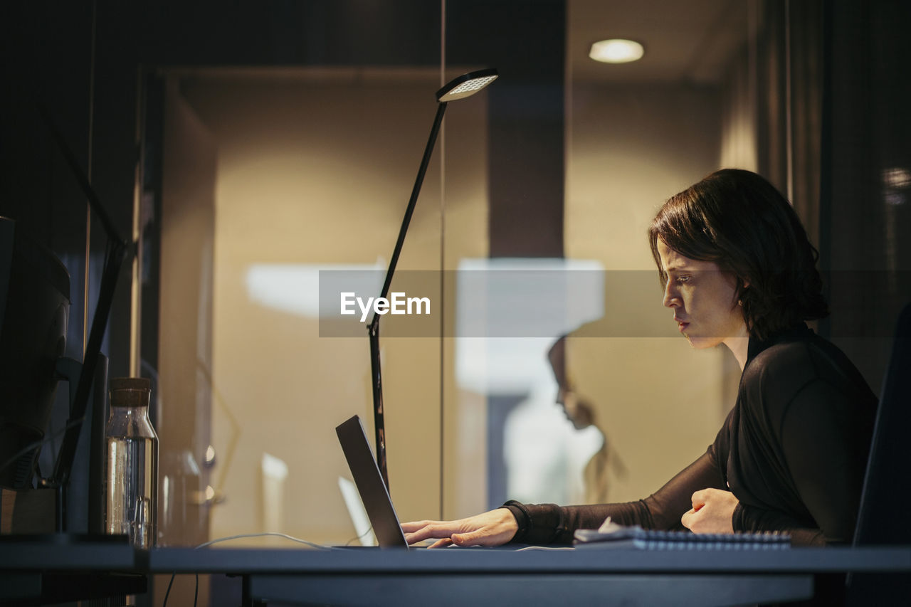 Side view of businesswoman using laptop at desk in dark office