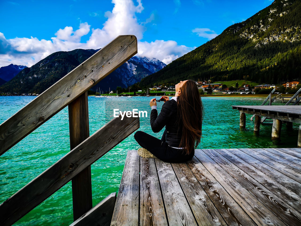 WOMAN SITTING BY RAILING AGAINST LAKE AND MOUNTAINS