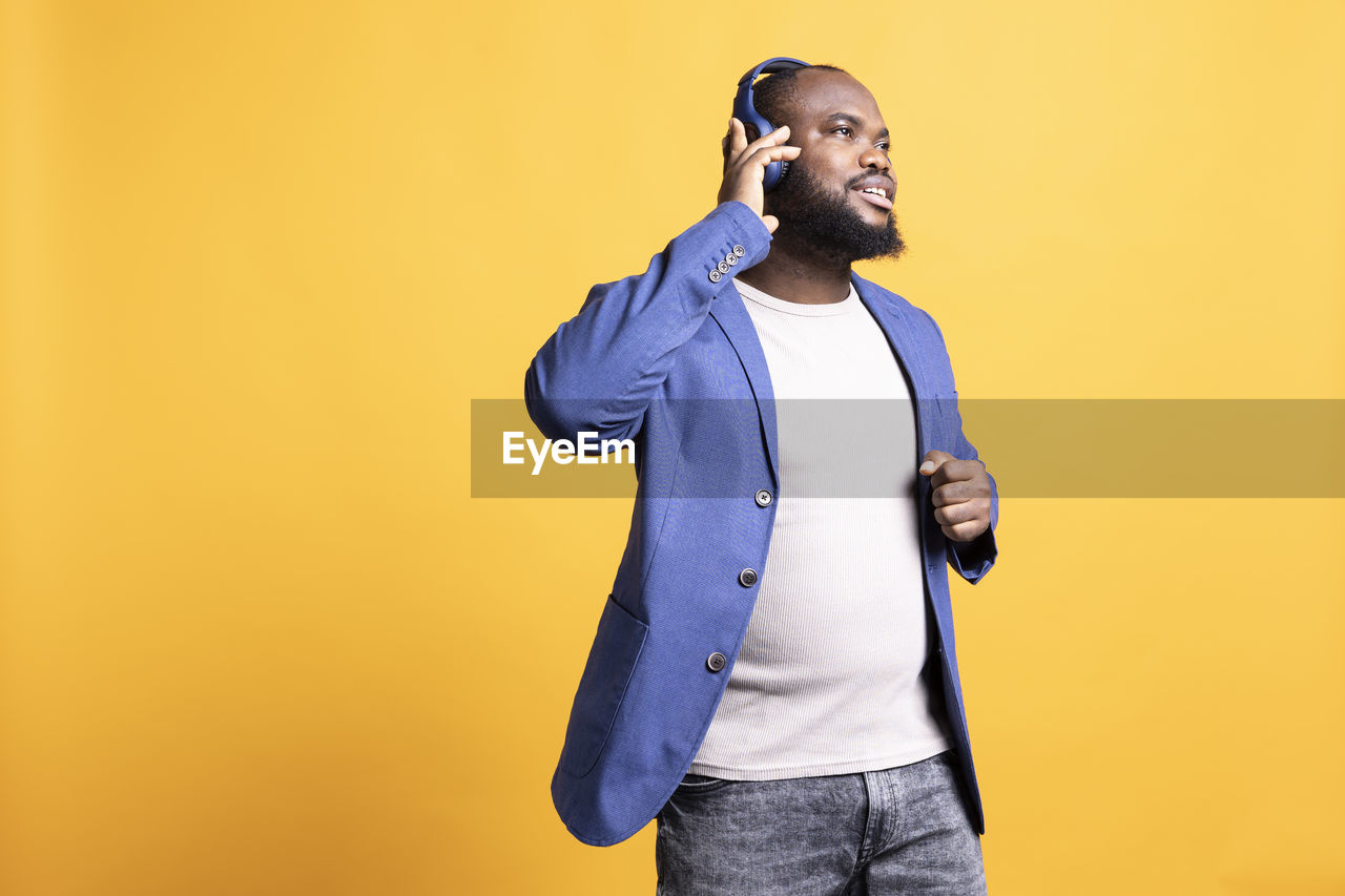 portrait of young man with arms crossed standing against yellow background