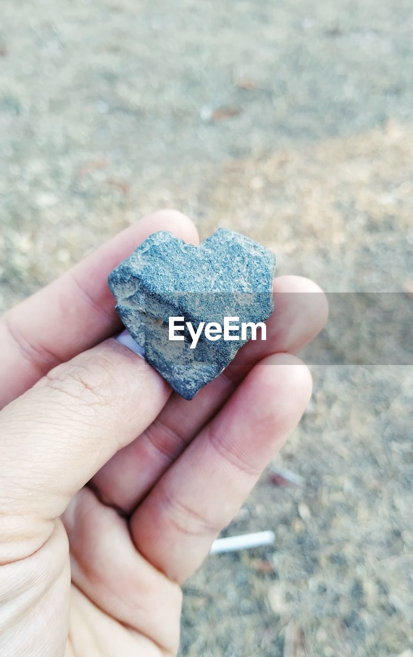 Cropped hand holding heart shape stone on field