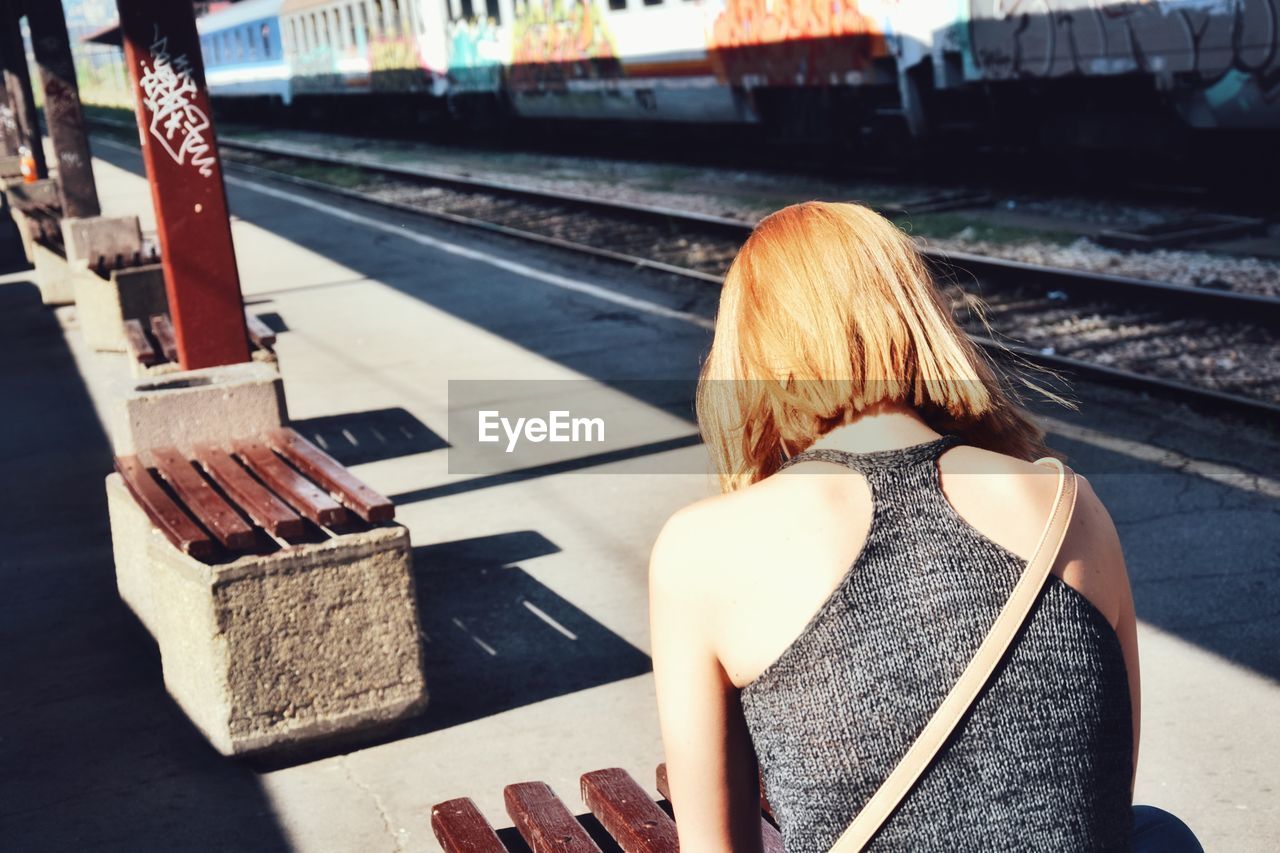 Rear view of woman sitting on railroad station platform