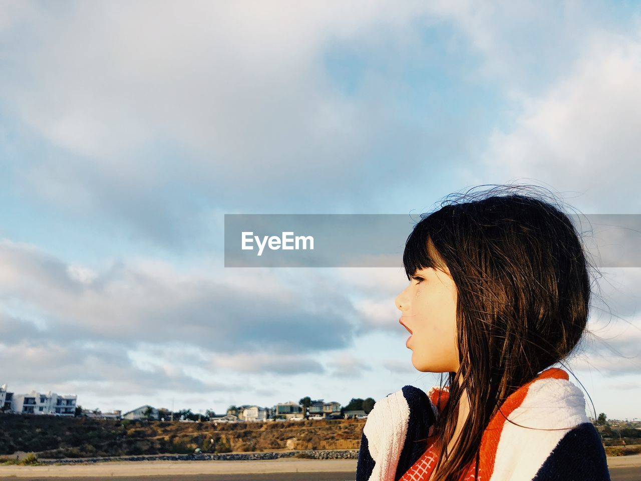 Close-up of girl looking away while standing against sky