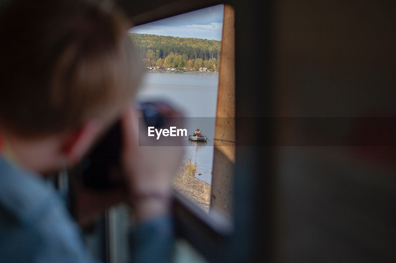 REAR VIEW OF WOMAN LOOKING AT WINDOW