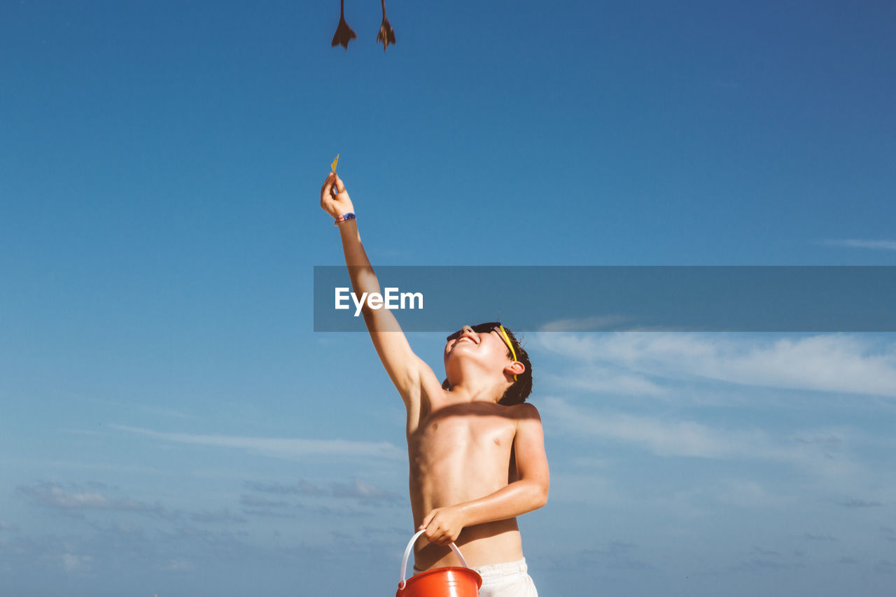 Low angle view of boy standing against blue sky