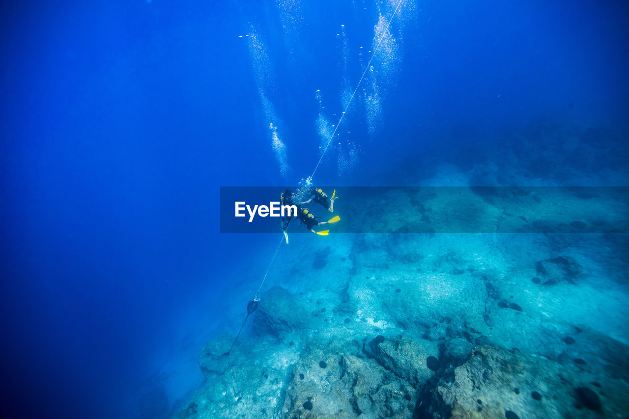 High angle view of scuba divers holding rope over rock while swimming undersea