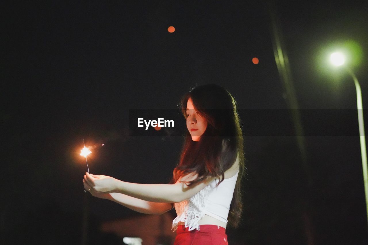 Beautiful woman holding sparkler at night