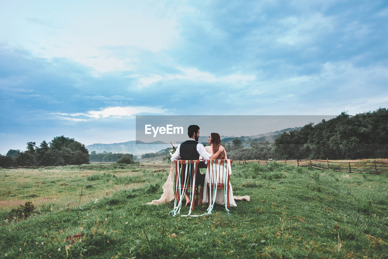 Rear view of wedding couple sitting on chairs at farm