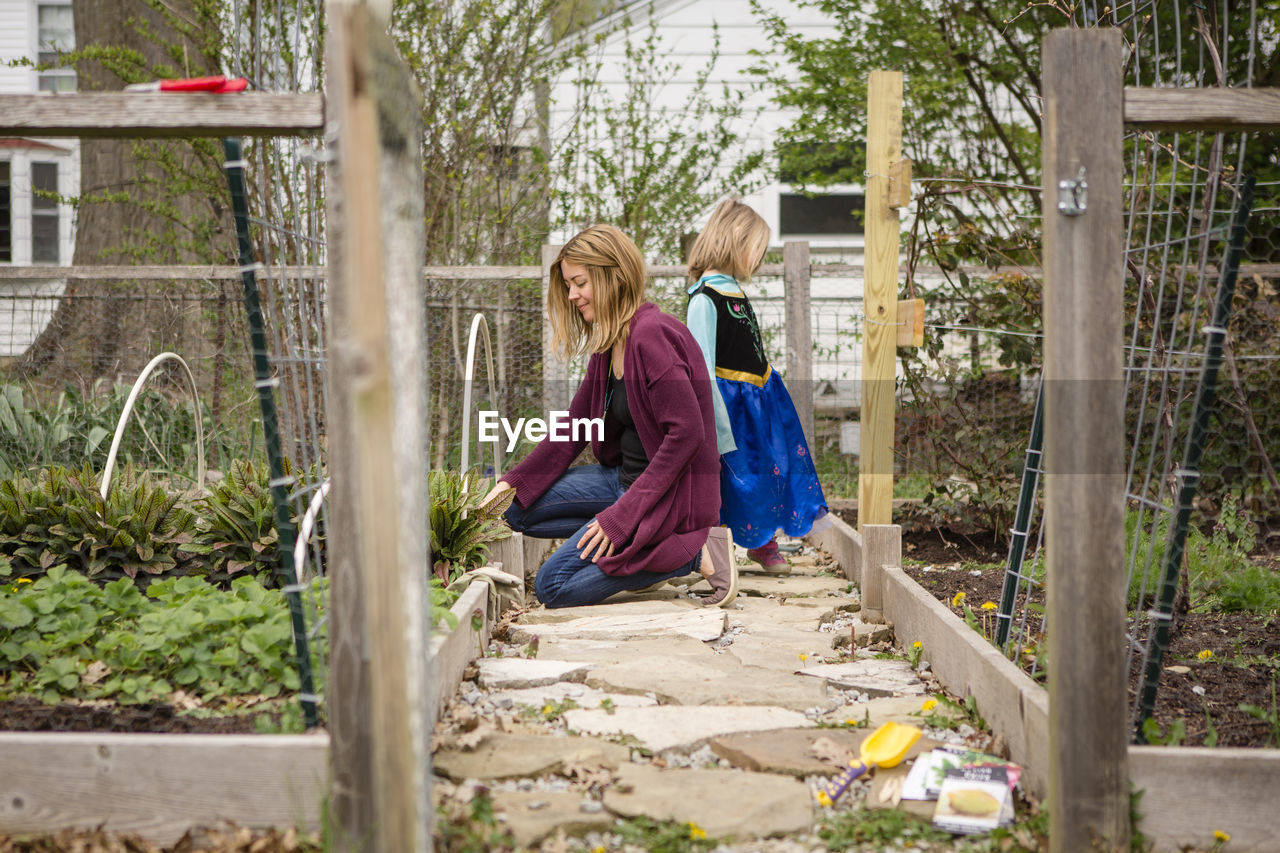 A mother works in her garden while a small child in costume stands by