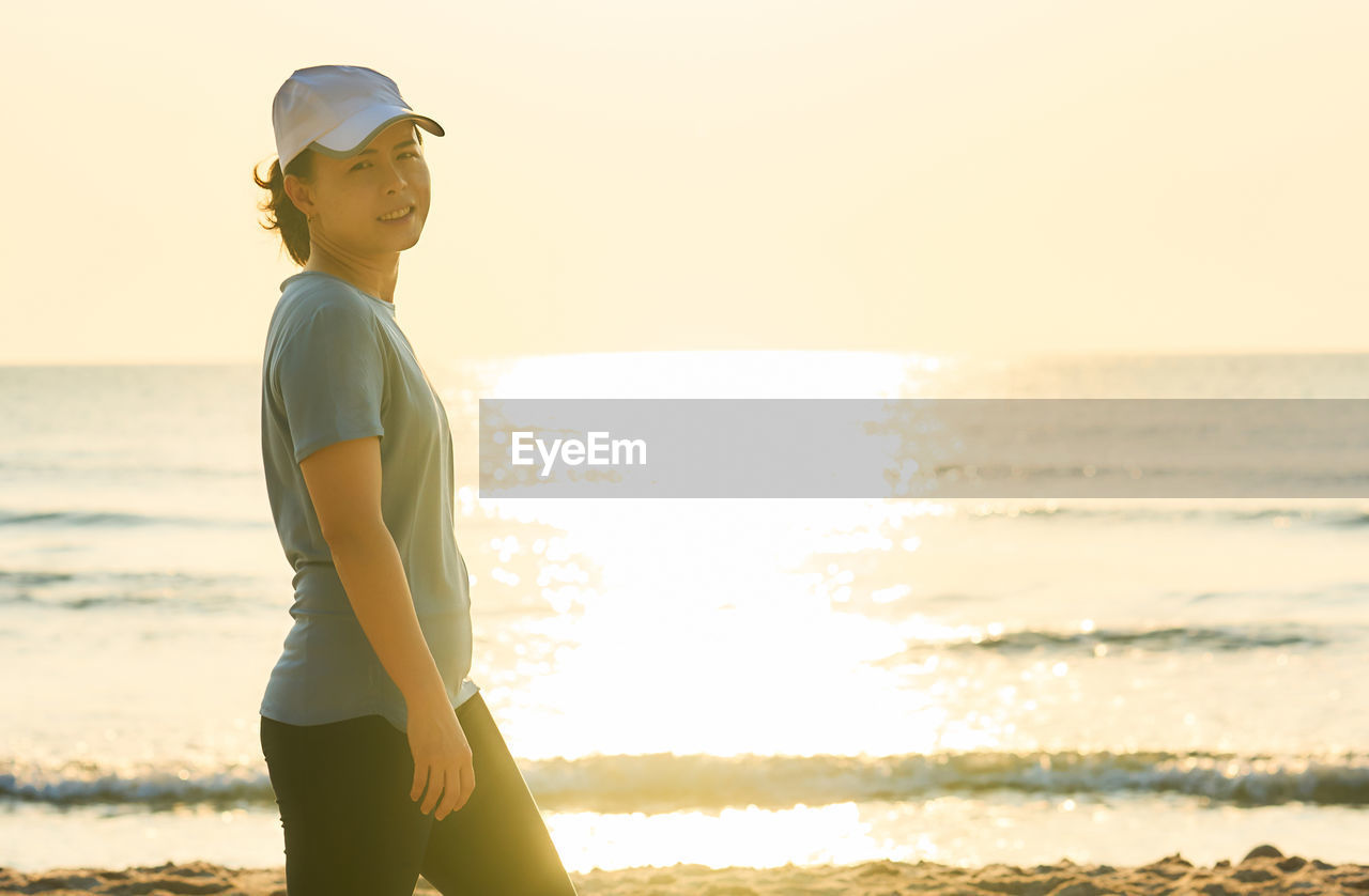 Portrait of woman walking at beach against clear sky during sunset