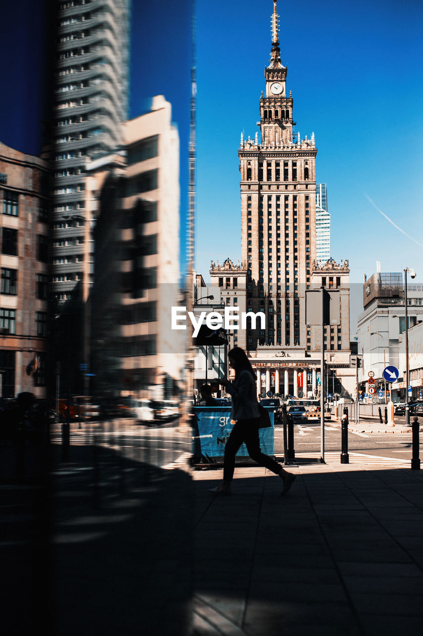 Side view of silhouette woman walking on street against buildings in city