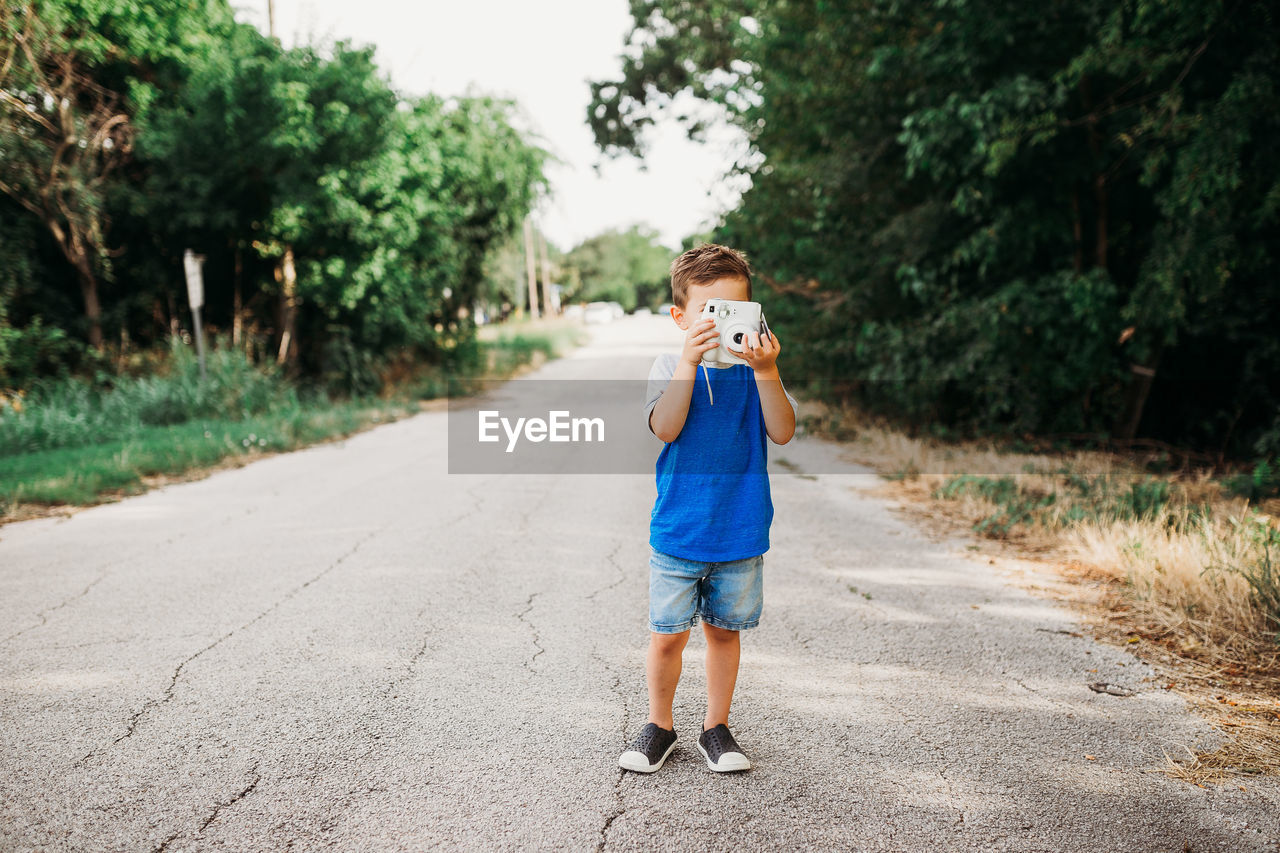 Young boy standing outside taking photo with instant camera