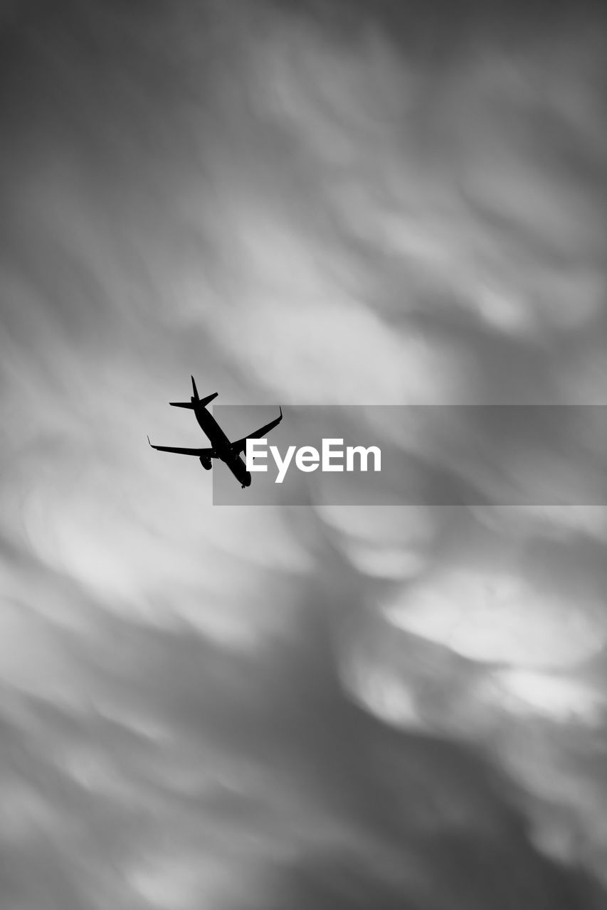 flying, sky, cloud, air vehicle, airplane, transportation, mode of transportation, black and white, low angle view, mid-air, monochrome, nature, travel, monochrome photography, silhouette, motion, overcast, on the move, no people, wing, journey, darkness, vehicle, outdoors, day, aircraft, dramatic sky
