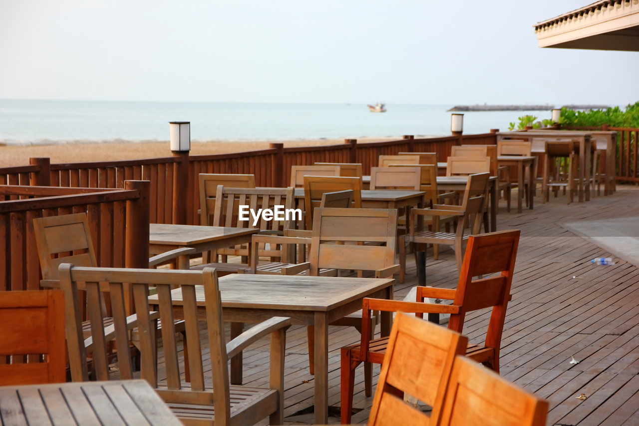 Empty chairs and tables at beach against sky