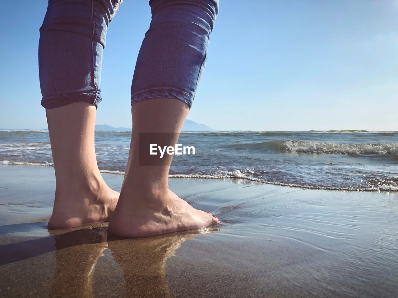 LOW SECTION OF WOMAN STANDING ON BEACH